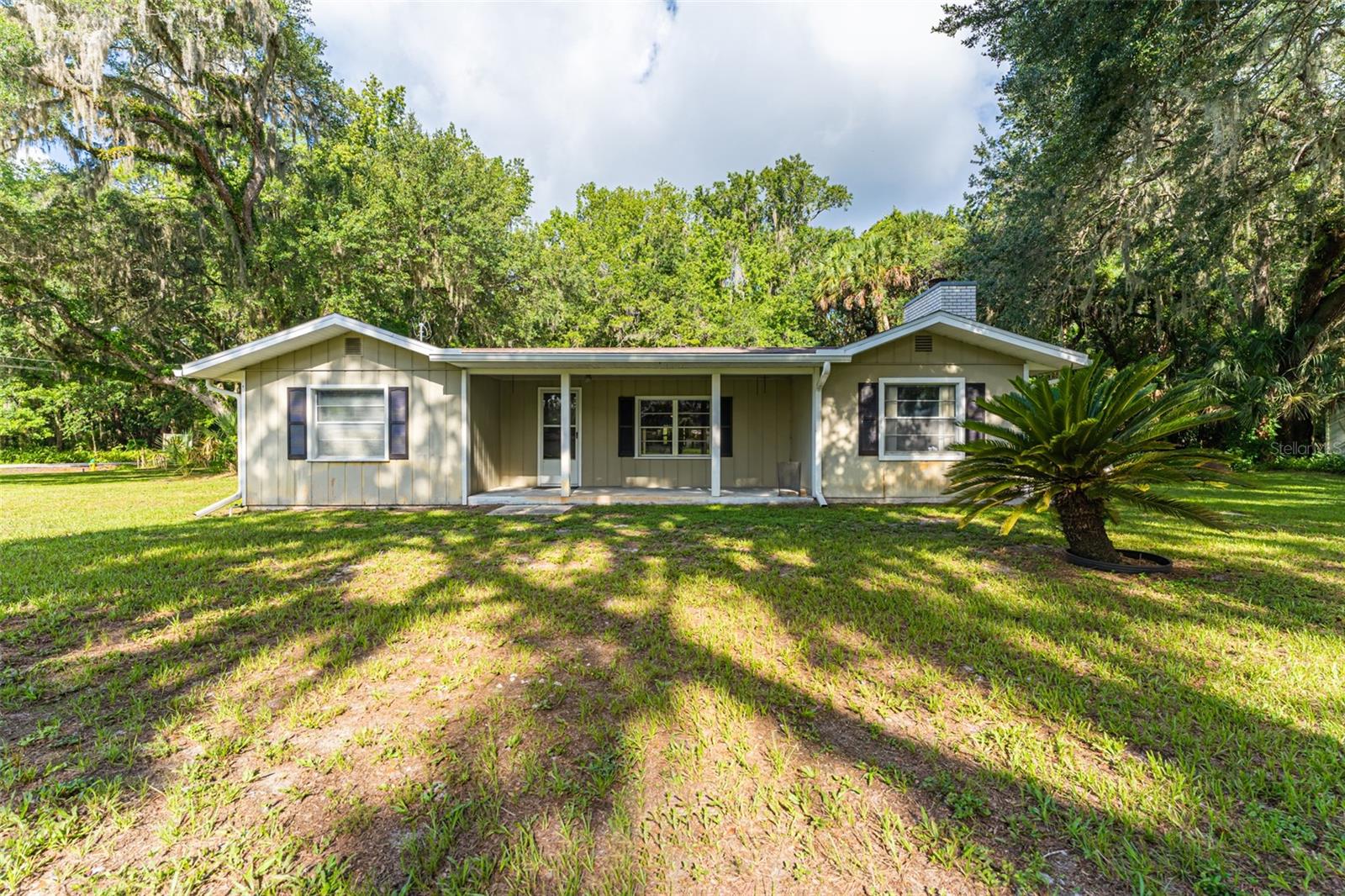 A single-story house with a front porch, surrounded by green grass and trees.