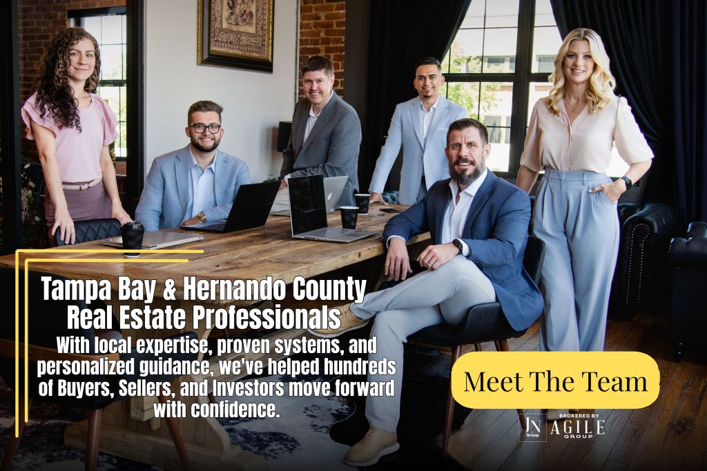 A group of six real estate professionals posing together in a stylish office space. They are smiling and dressed in business attire, promoting their services in Tampa Bay and Hernando County.